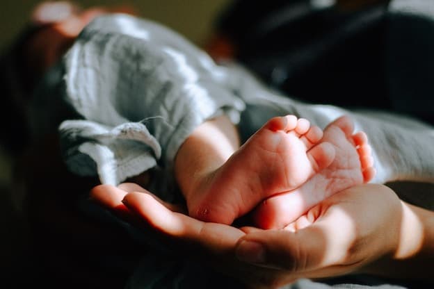 Tender tiny newborn feet resting softly in loving hands