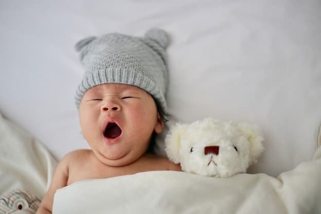 Adorable newborn baby yawning in cozy knit bear hat with teddy