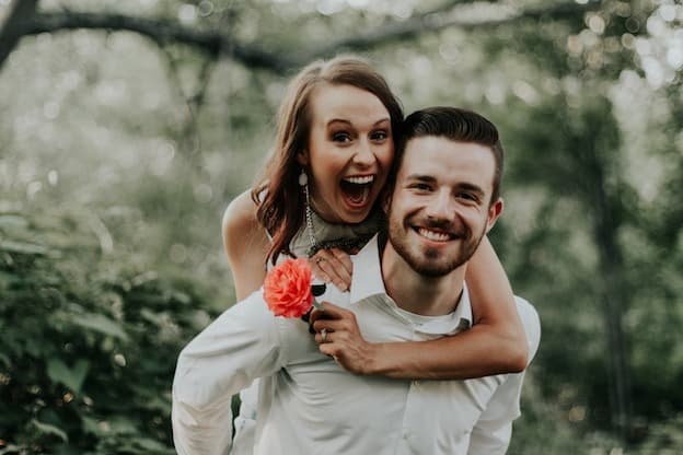 Playful honeymoon couple laughing with flower outdoors